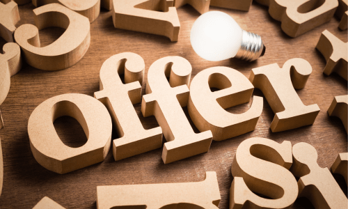The word 'offer' spelled out in wooden letters with a glowing lightbulb placed on top.